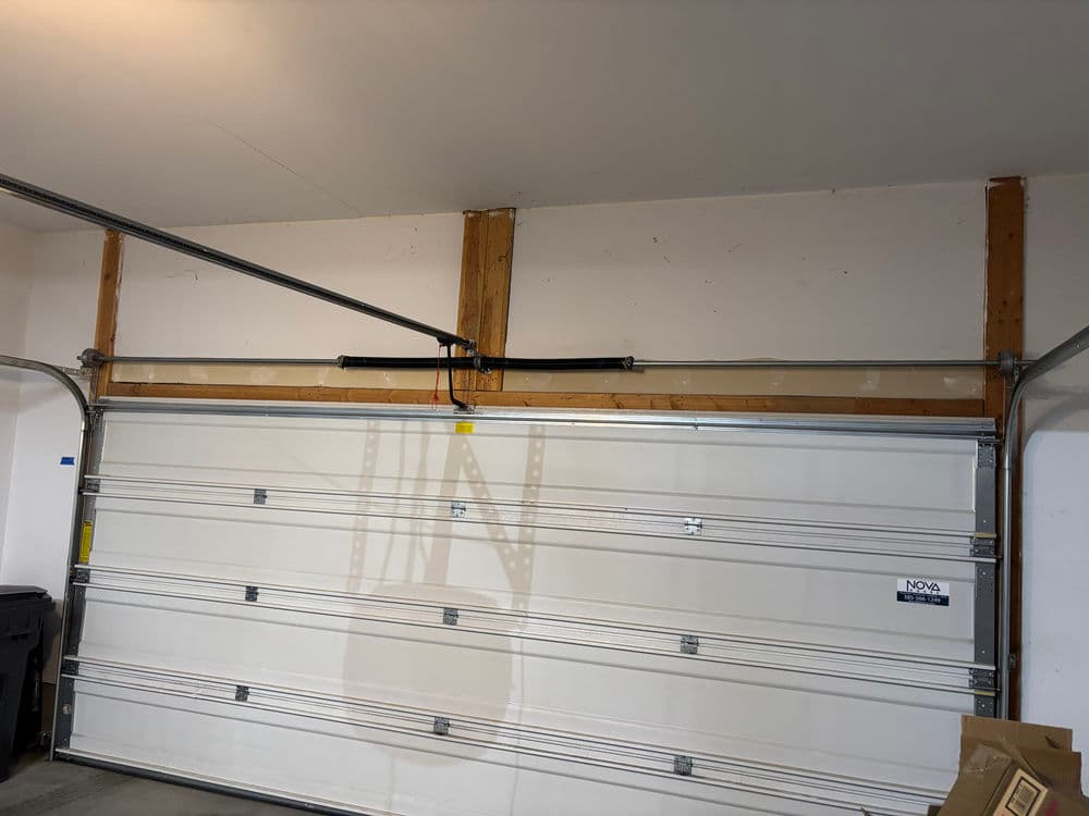 White garage door installed in a garage with wooden support beams and metal tracks.