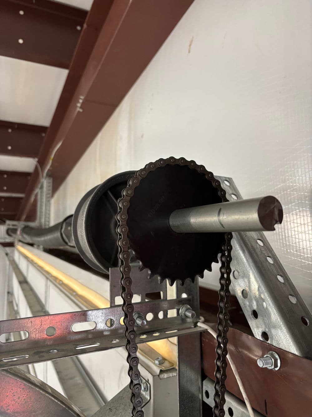 Industrial overhead roller system with chain and sprocket mounted on metal track.