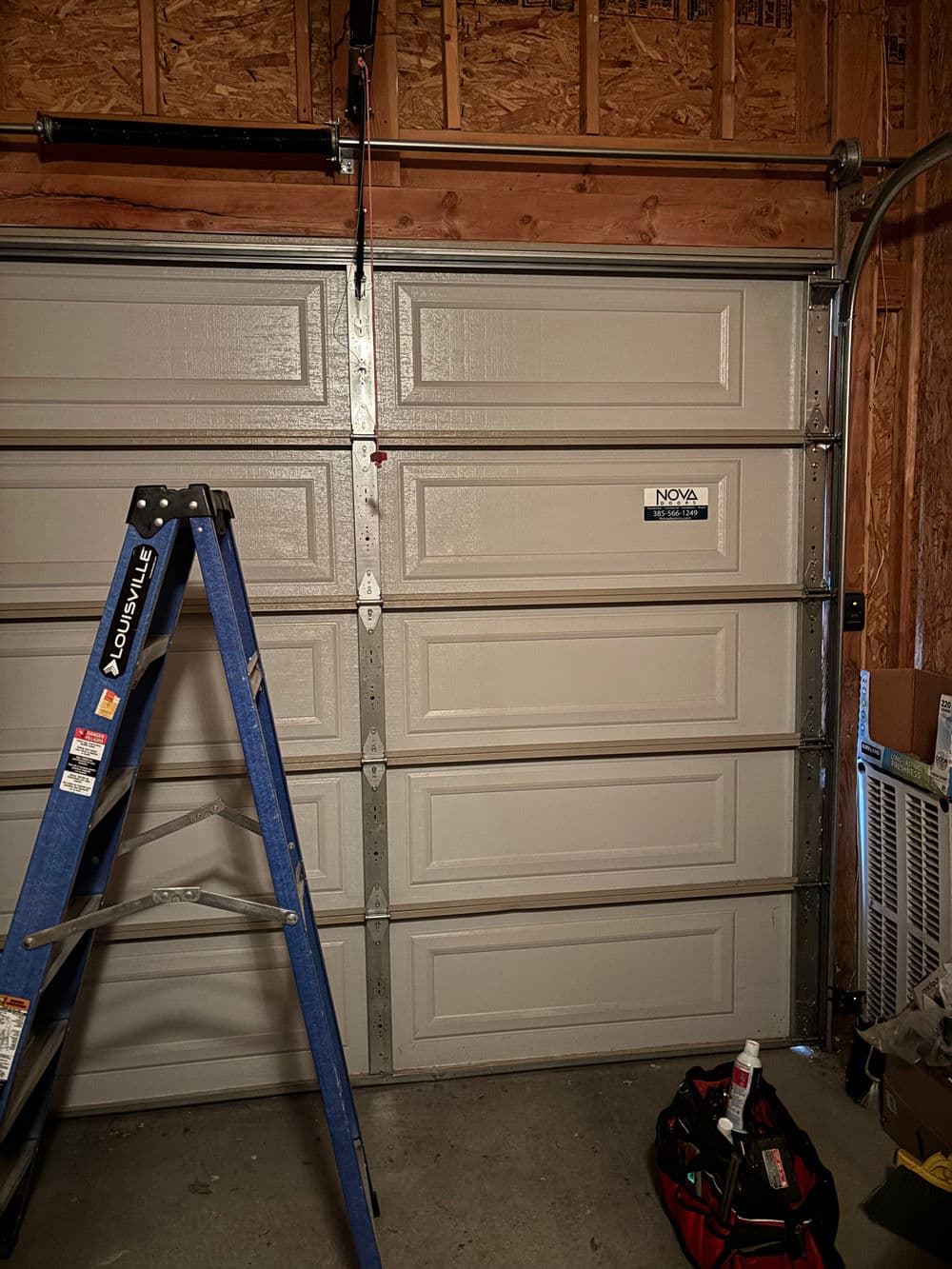 Interior of a garage with a ladder, tool bag, and closed garage door.