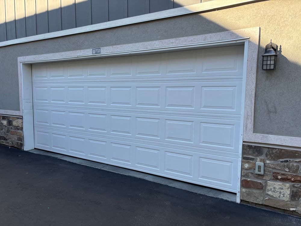 White garage door on a grey building with stone accents and outdoor lighting.
