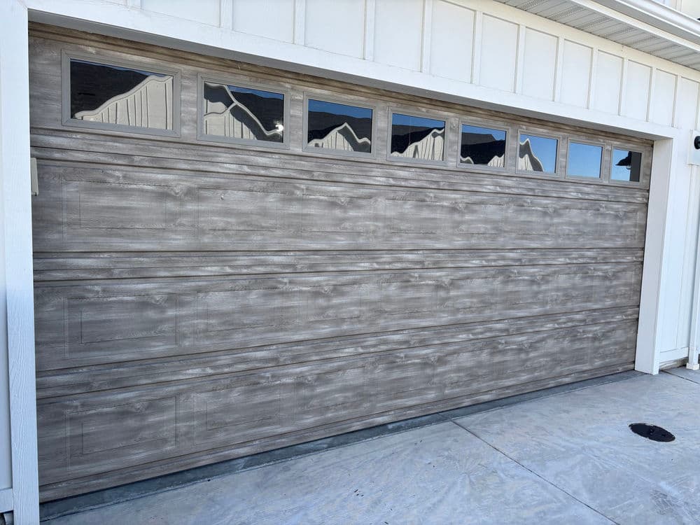 Modern wooden garage door with glass panels, installed on a residential home exterior.