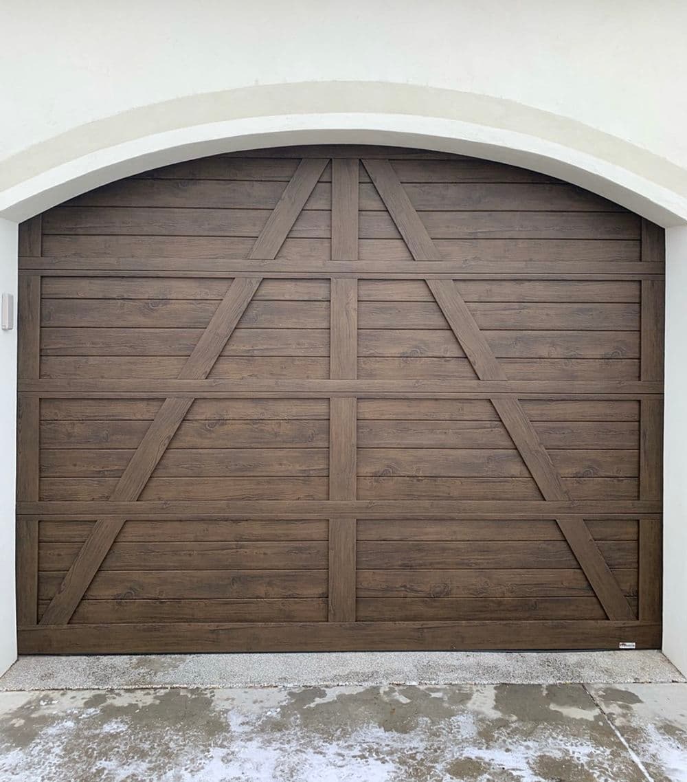 Wooden garage door with a sleek design and arched top, set against a light-colored wall.