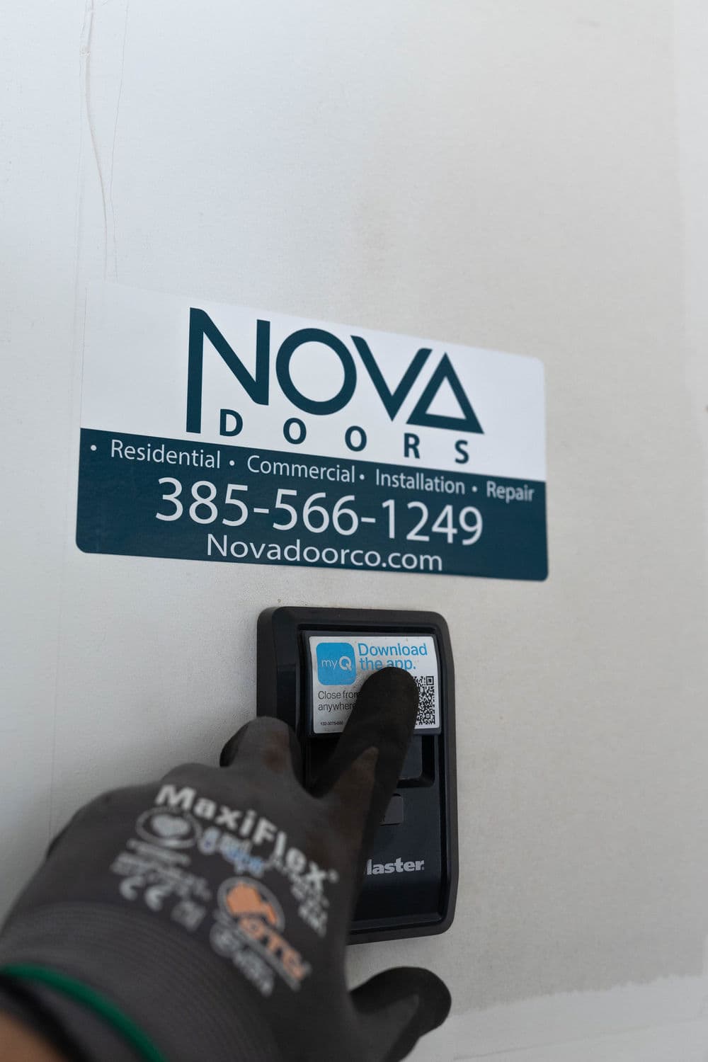 Hand pressing a keypad for NOVA Doors, featuring contact information and a QR code.