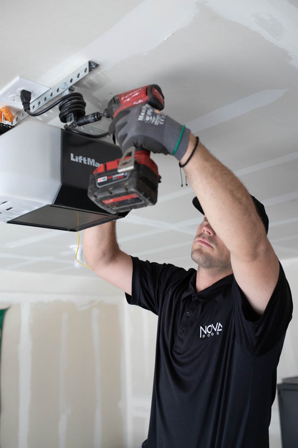 Technician installing a LiftMaster garage door opener with a power drill in a home garage.