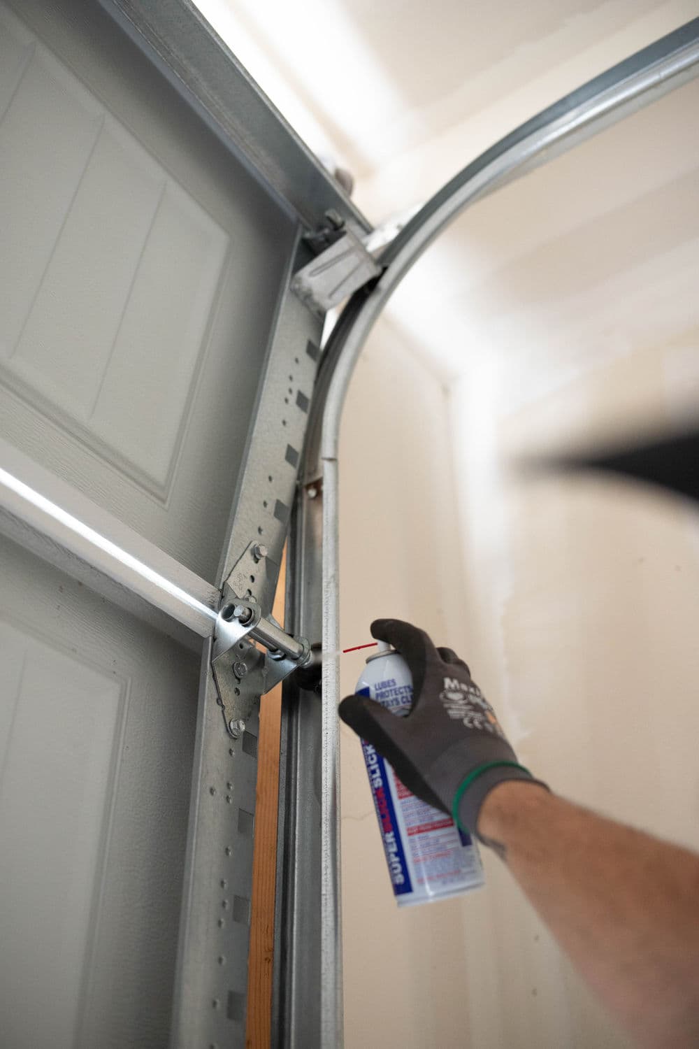 Person applying lubricant to a garage door track for maintenance and smooth operation.