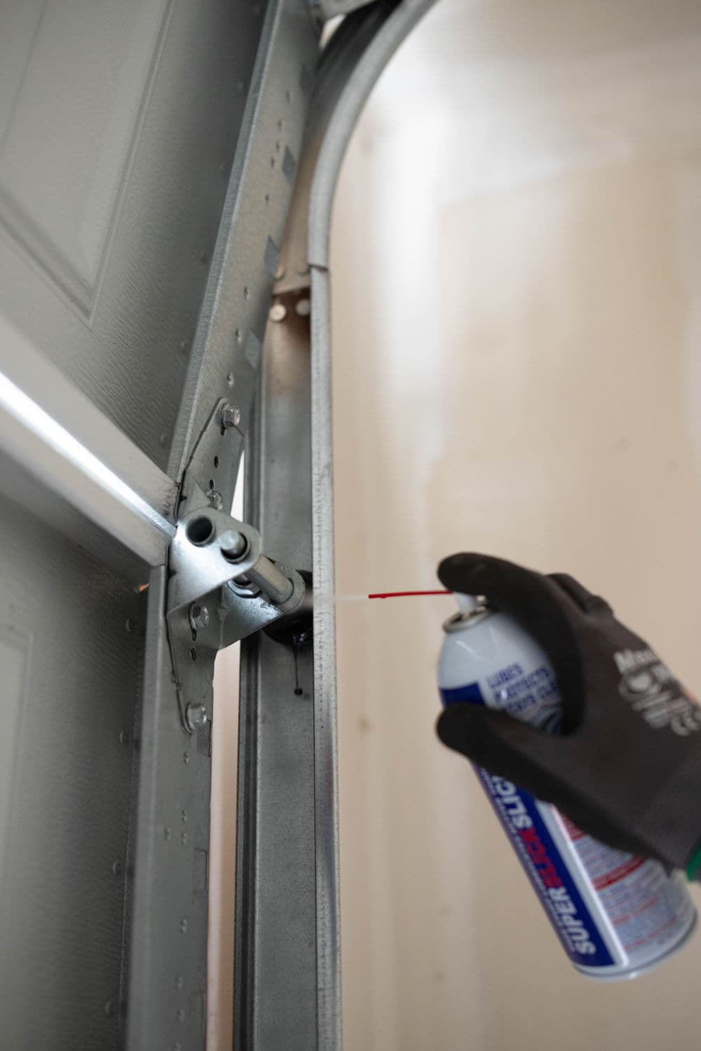 Person applying lubricant to a garage door hinge for maintenance and smooth operation.