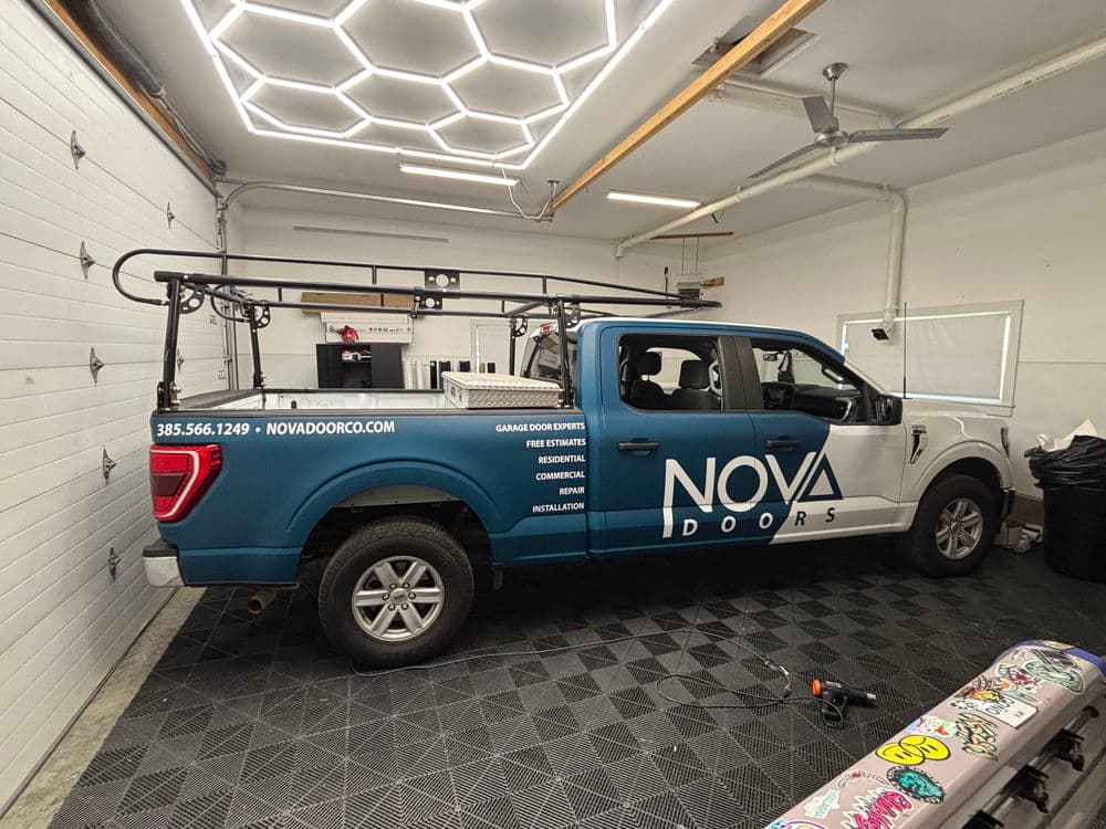 NOVA Doors branded truck in a garage with a ladder rack and garage door equipment.