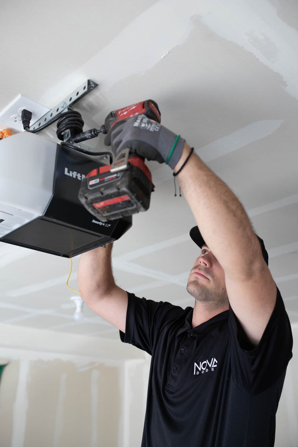 Technician installing a LiftMaster garage door opener with a power drill.