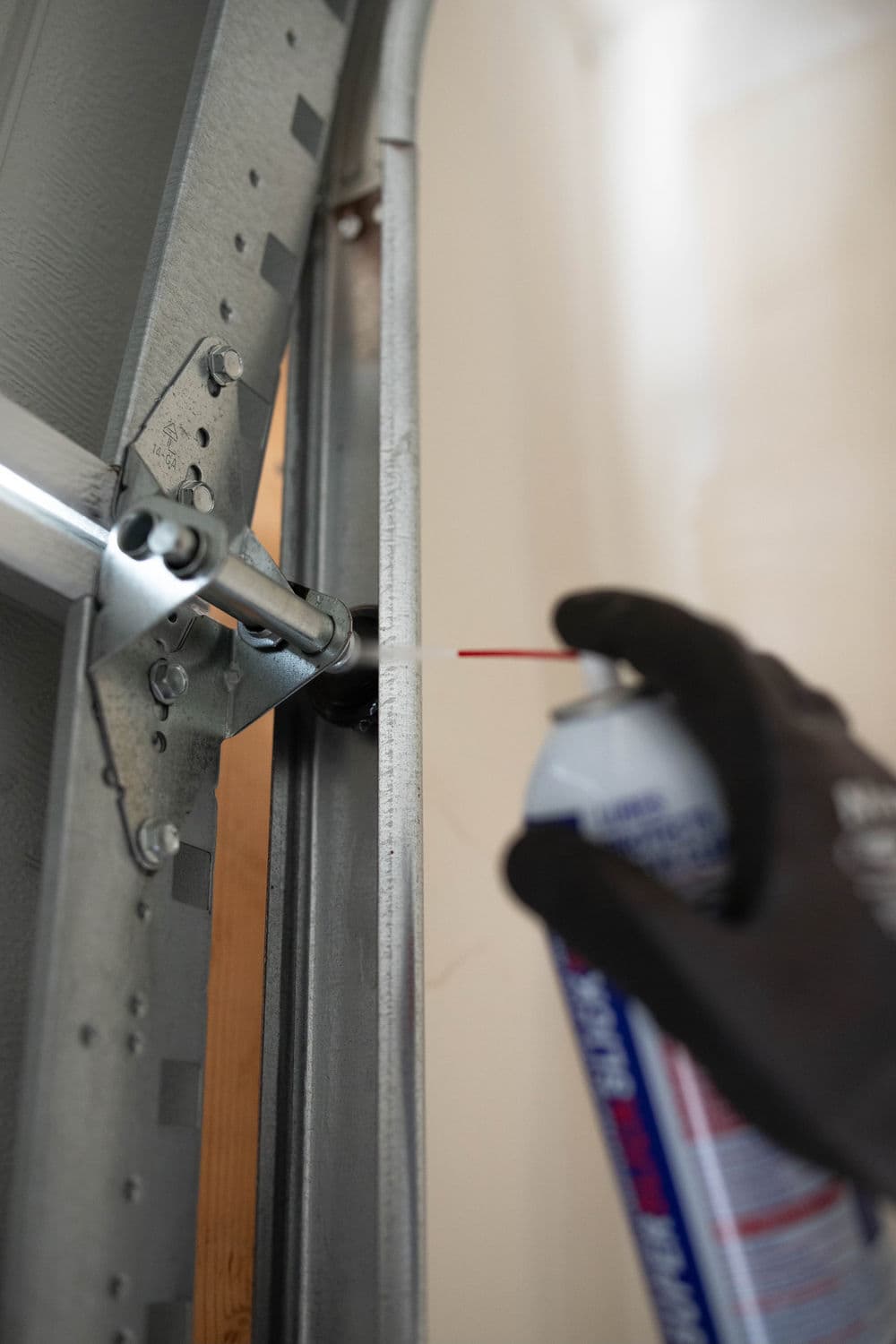 Person lubricating a garage door track with spray grease for maintenance.