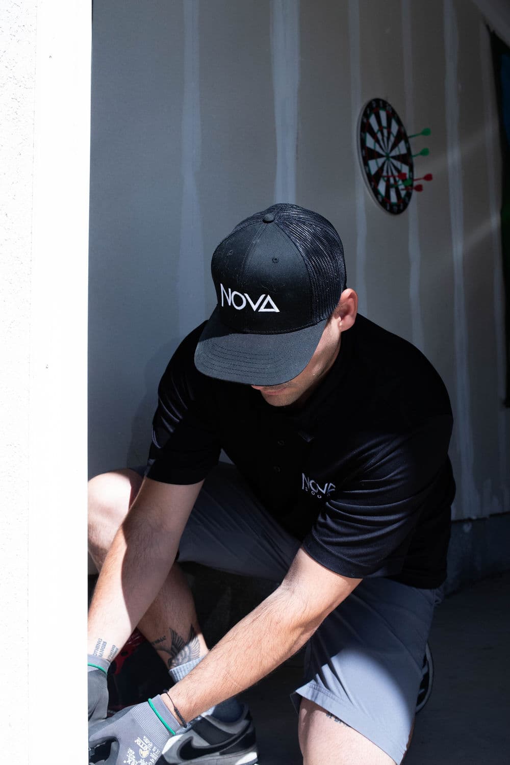 Person in a black NOVA cap and shirt working indoors near a dartboard.